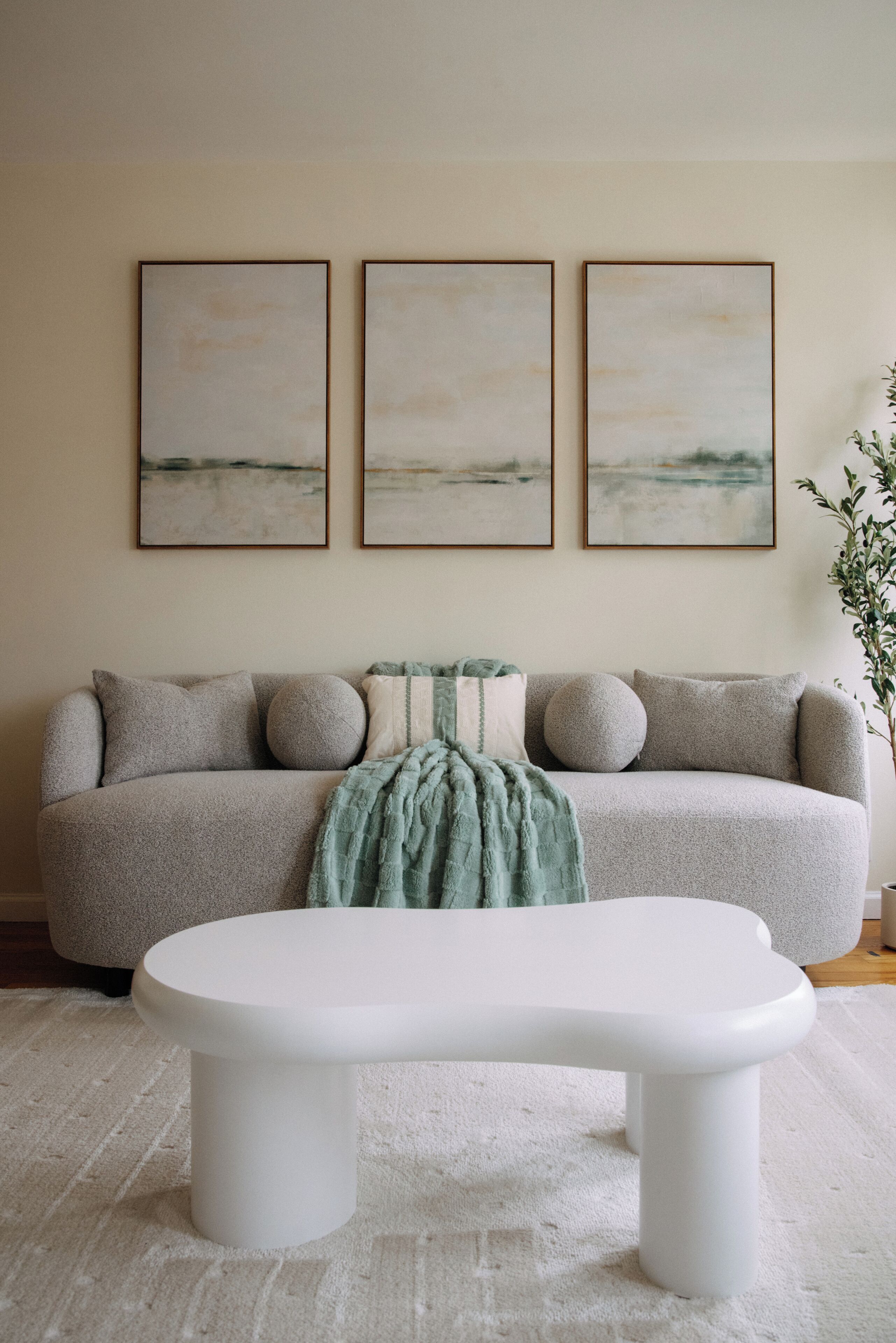 A living room with a sofa, a white coffee table, and three framed artworks on the wall.