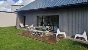 Una casa moderna con techo de metal, un patio con mesa y sillas, y un jardín cubierto de césped.