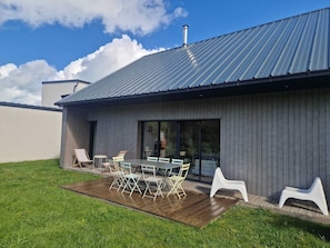 A modern house with a metal roof, a patio with a table and chairs, and a grassy lawn. - House Les Dunes Bourgales (Gouville-sur-Mer)