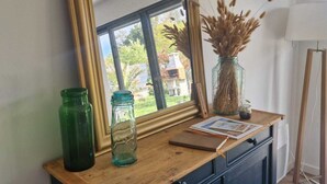 Un mueble de madera con un espejo, un frasco de vidrio verde y un jarrón con plantas secas.