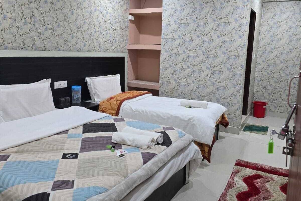 A hotel room with two beds, a large window, a red rug, and a bathroom with a shower.