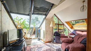 Quarto acolhedor com uma cama, uma televisão, uma planta e uma janela grande.