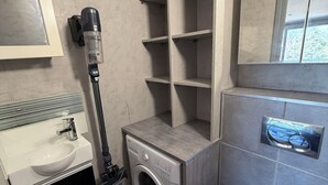 Een kleine badkamer met een wastafel, toilet, wasmachine en stofzuiger.