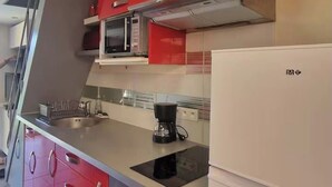 Een keuken met rode kastjes, een magnetron, een fornuis en een koelkast.