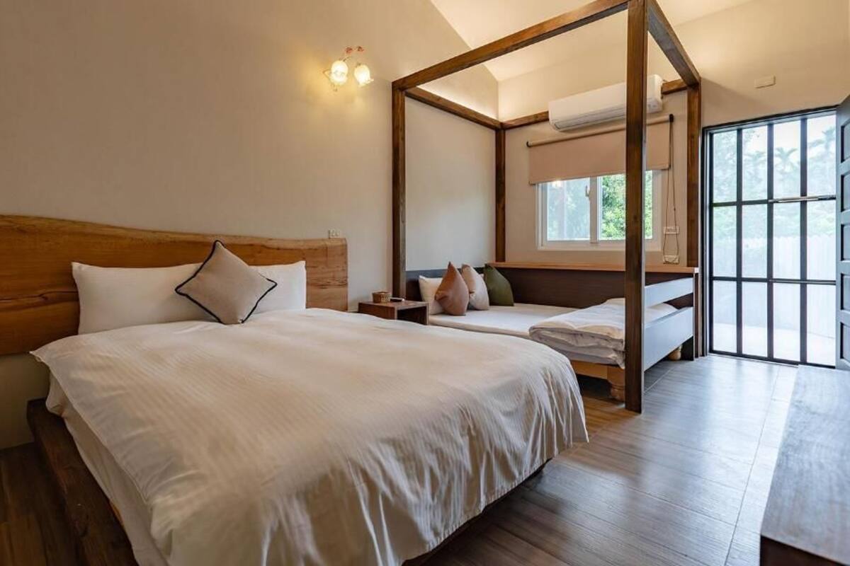 A bedroom with a large bed, a smaller bed, a wooden headboard, a nightstand, and a window with a view.