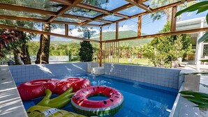 An indoor swimming pool with clear glass walls, surrounded by a tiled deck, and equipped with inflatable pool toys. - sun on the cloud (Shoufeng)