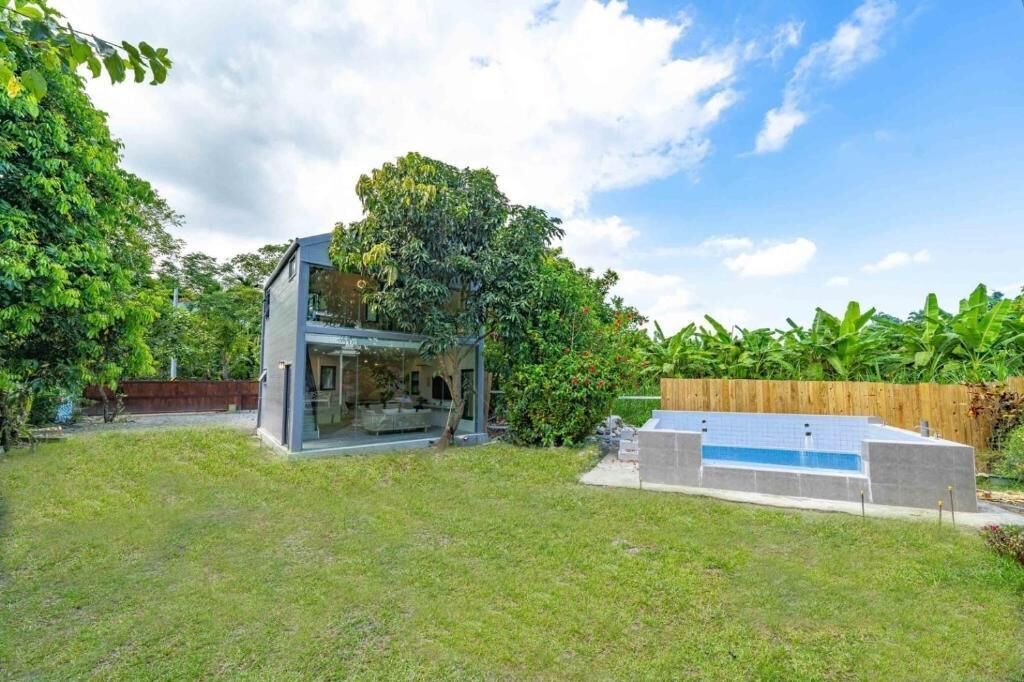 A modern house with a glass-enclosed patio, a swimming pool, and lush greenery.