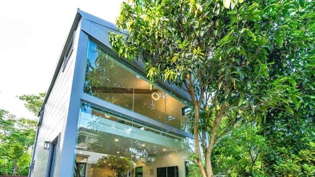 A modern two-story building with large glass windows, a visible outdoor seating area, and a tree in the foreground. - sun on the cloud (Shoufeng)