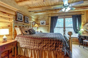 A wooden cabin bedroom with a bed, a desk, a chair, a ceiling fan, and a window with curtains. - Groups Welcome! Cozy Creek-Front Cabin in Old Fort (Old Fort)
