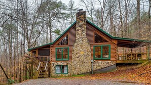Une cabane en rondins avec une cheminée en pierre, un revêtement extérieur en bois et un escalier menant à une terrasse.