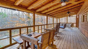 Une terrasse en bois avec une table et des chaises, un ventilateur de plafond et une vue sur les arbres.