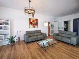 Una sala de estar moderna con dos sofás grises, una mesa de centro de vidrio, piso de madera, una lámpara de techo y un cuadro en la pared.