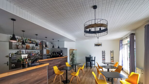 A modern bar area with a wooden counter, yellow chairs, and a coffee machine. - Hôtel Restaurant le Tanargue (Valgorge)