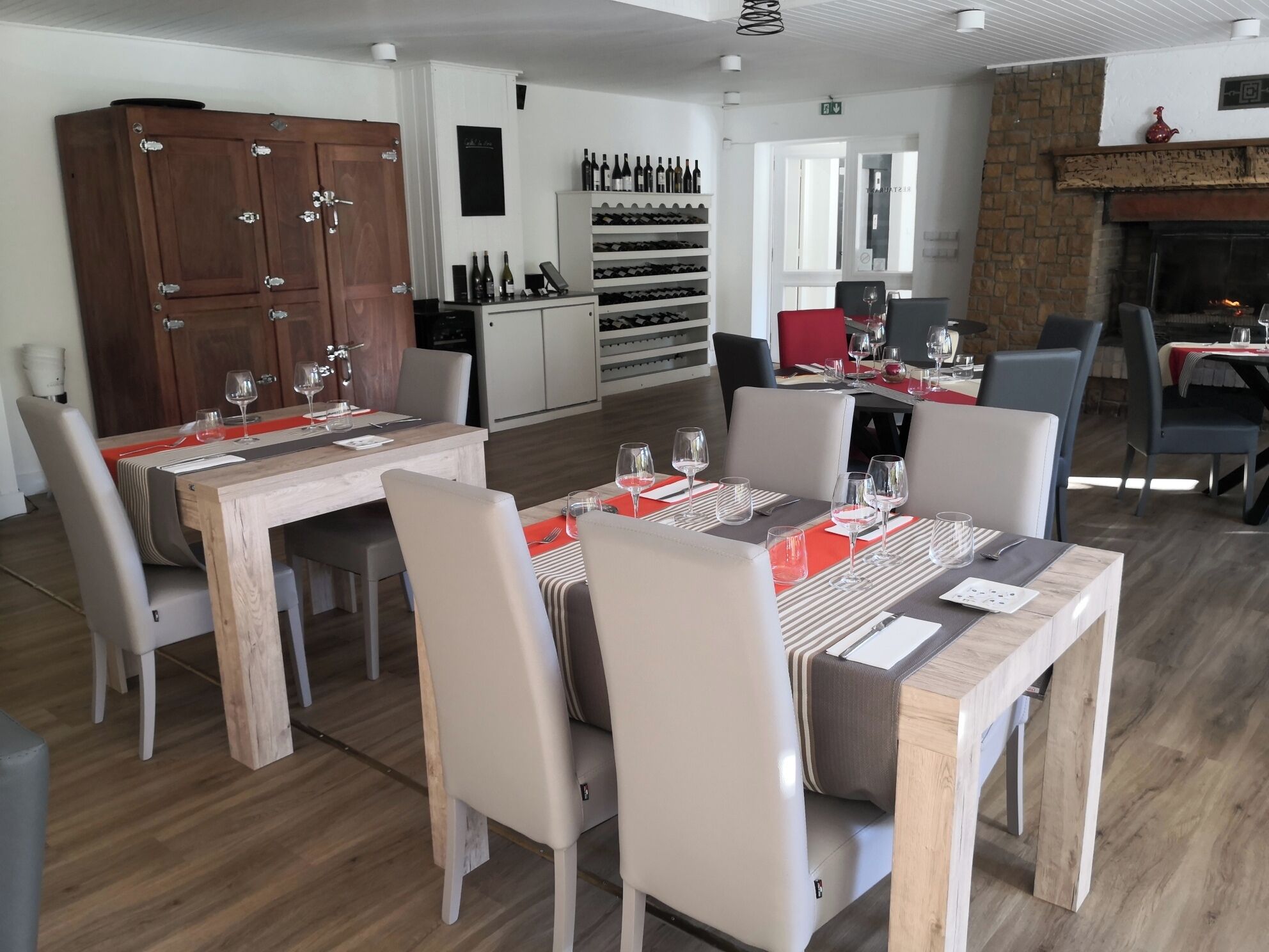 A dining area with wooden tables and chairs, a wine rack, and a fireplace.