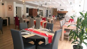 A restaurant with multiple dining tables, chairs, and hanging pendant lights. - Hôtel Restaurant le Tanargue (Valgorge)