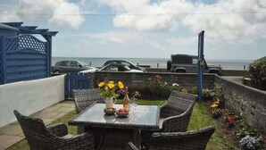 Eine Terrasse mit Korbmöbeln, einem Tisch mit Blumenvase und Blick auf das Meer.