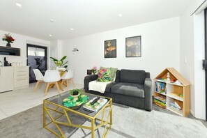 A modern living room with a sofa, coffee table, and a bookshelf. - Spacious 2BR Townhouse with Yard Wilmer Street (Christchurch)