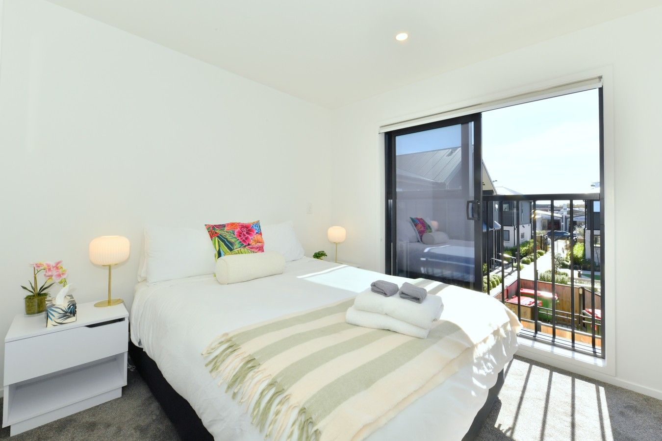 A modern bedroom with a large bed, bedside tables, a window with a view, and a balcony.