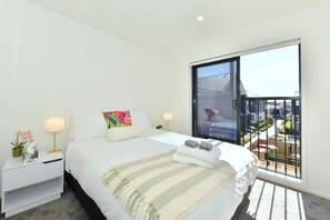 Ein modernes Schlafzimmer mit einem großen Bett, Nachttischen, einem Fenster mit Blick und einem Balkon.