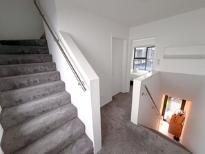 Eine Treppe führt zu einer Zwischenebene mit Blick auf einen Raum, der ein Bett und ein Fenster zeigt.