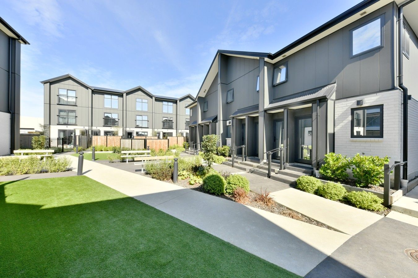 A modern residential building with a courtyard, featuring a central pathway, benches, and small landscaped areas.