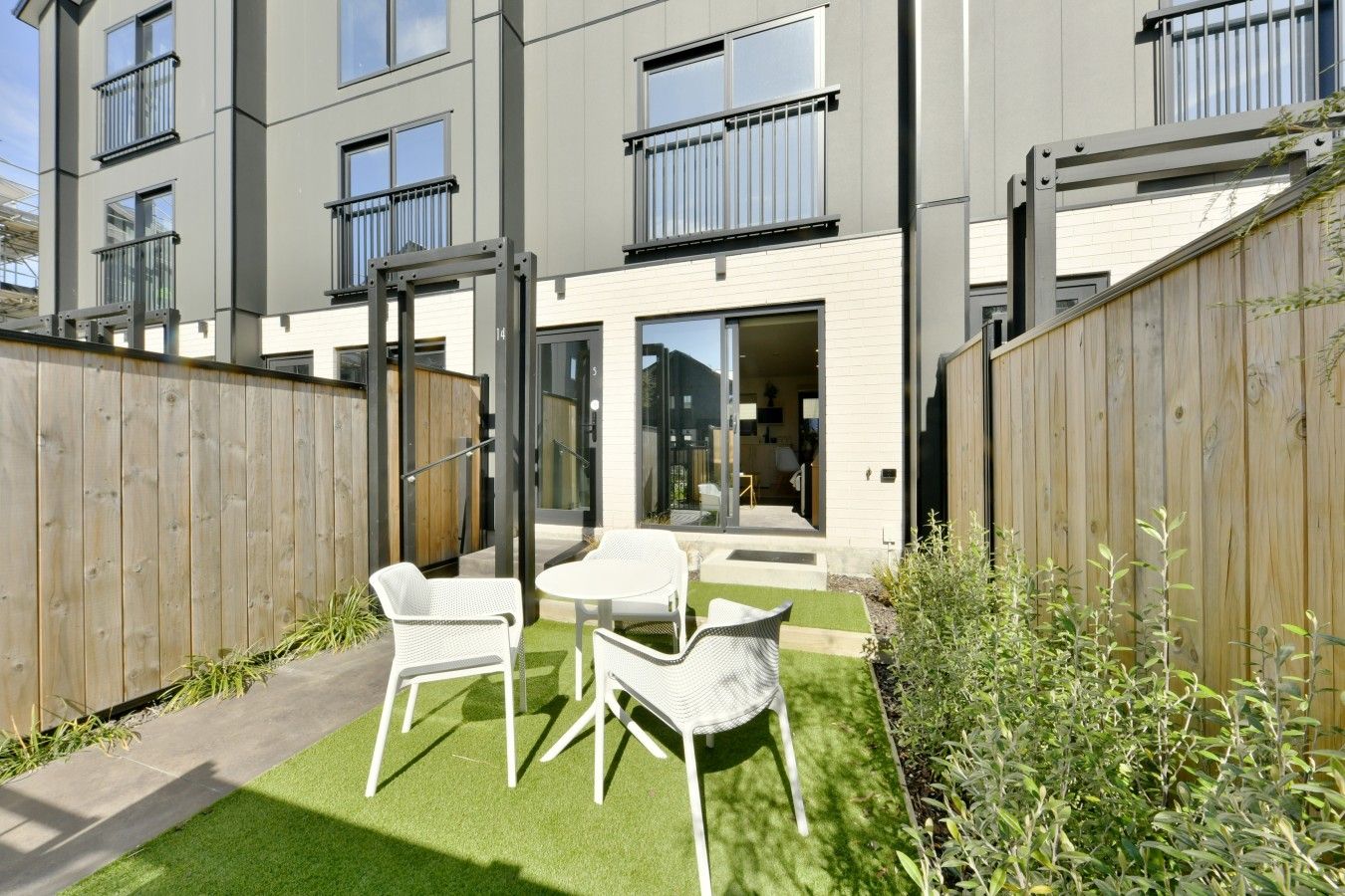 Un edificio de apartamentos moderno con un patio amoblado con muebles de exterior y un cerco de madera.