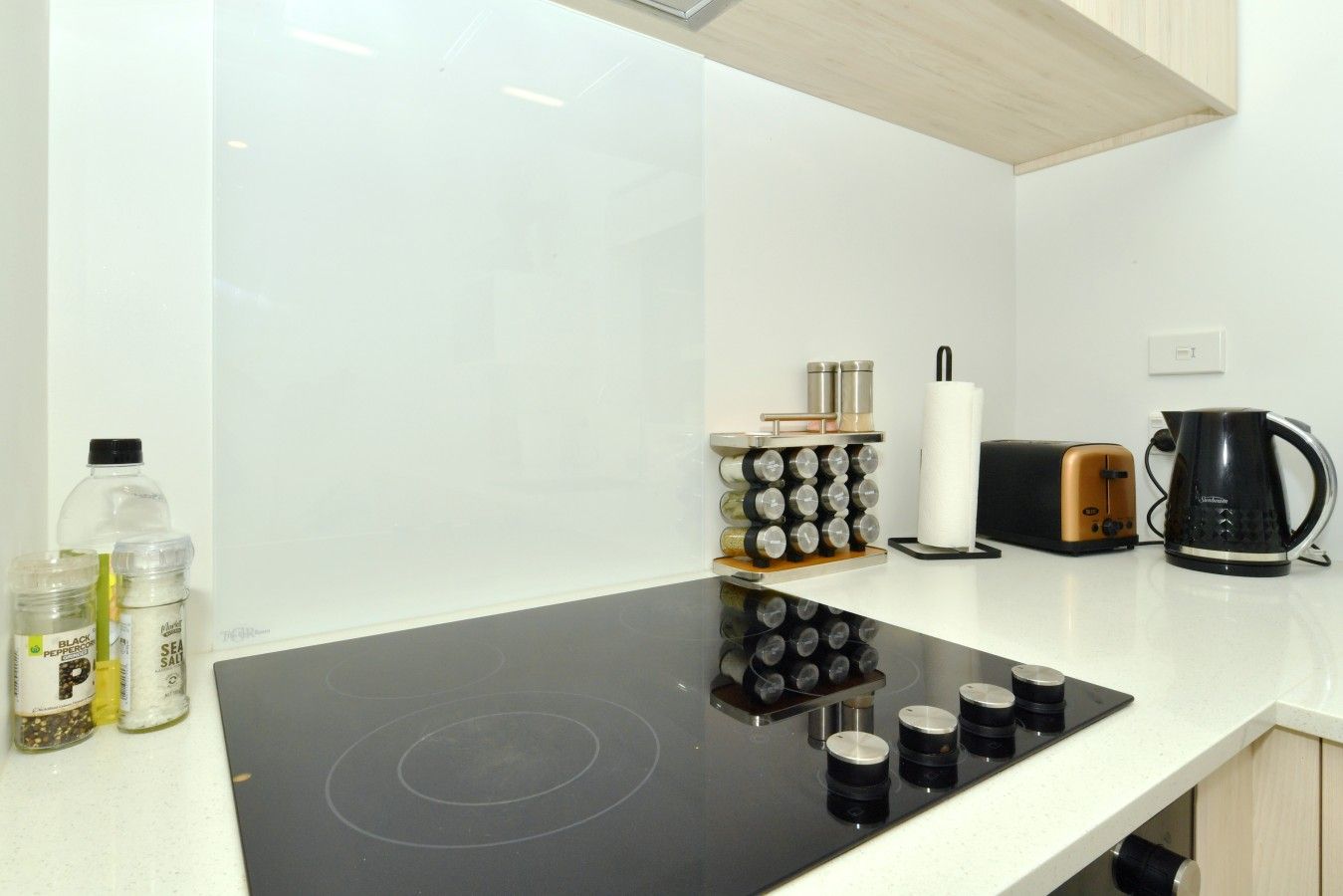 A modern kitchen with a black induction cooktop, a coffee maker, and a spice rack.