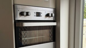 Cucina con forno integrato, pannello di controllo digitale e finestra che mostra una recinzione in legno.