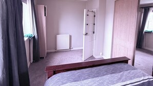 Una camera da letto con un letto, un termosifone, una porta e una finestra con tende.