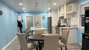 A modern kitchen with white cabinets, a dining area with a round table and chairs, and a person working near a door. - Indy Michigan rd house in northwest of Indianapolis near 465 north, 4brds 3 bath (Indianapolis)
