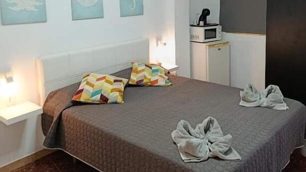 A bedroom with a bed, two wall-mounted lamps, a nightstand, a small table, and three wall art pieces.