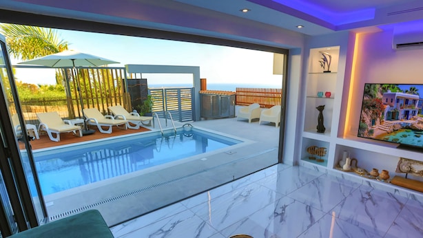 Een moderne binnenzwembadruimte met lounge stoelen, een overdekt zwembad en uitzicht op zee.