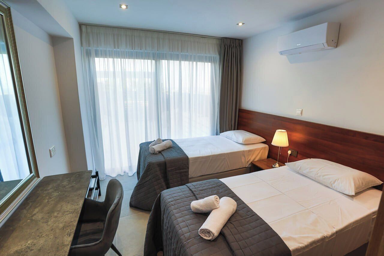 Une chambre d’hôtel avec deux lits, un bureau, une chaise, une lampe et un grand miroir.