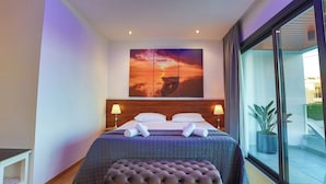 Een moderne hotelkamer met een groot bed, twee nachtkastjes, een groot raam en een schilderij van een zonsondergang aan de muur.