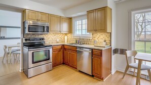 A kitchen with wooden cabinets, stainless steel appliances, and a window with a view of the outdoors. - Sandusky Adventure Hub: Patios, Grill + Yard! (Sandusky)