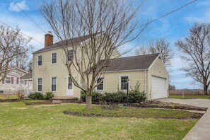 Une maison à deux étages avec un garage, un arbre dans le jardin et un ciel dégagé.