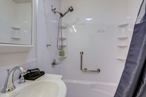 Une salle de bain équipée d’un lavabo, d’un miroir, d’une douche et de barres d’appui.