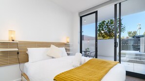 A hotel room with a bed, bedside lamps, a window, and a view of the outside. - Griffith Apartment | Prime Location+Courtyard+Gym (Griffith)