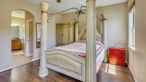 Un lit à baldaquin, un ventilateur de plafond en bois et une table de chevet rouge.