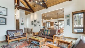 Amplia sala de estar con un tapete grande, sofás de cuero, mobiliario de madera y una cocina al fondo.