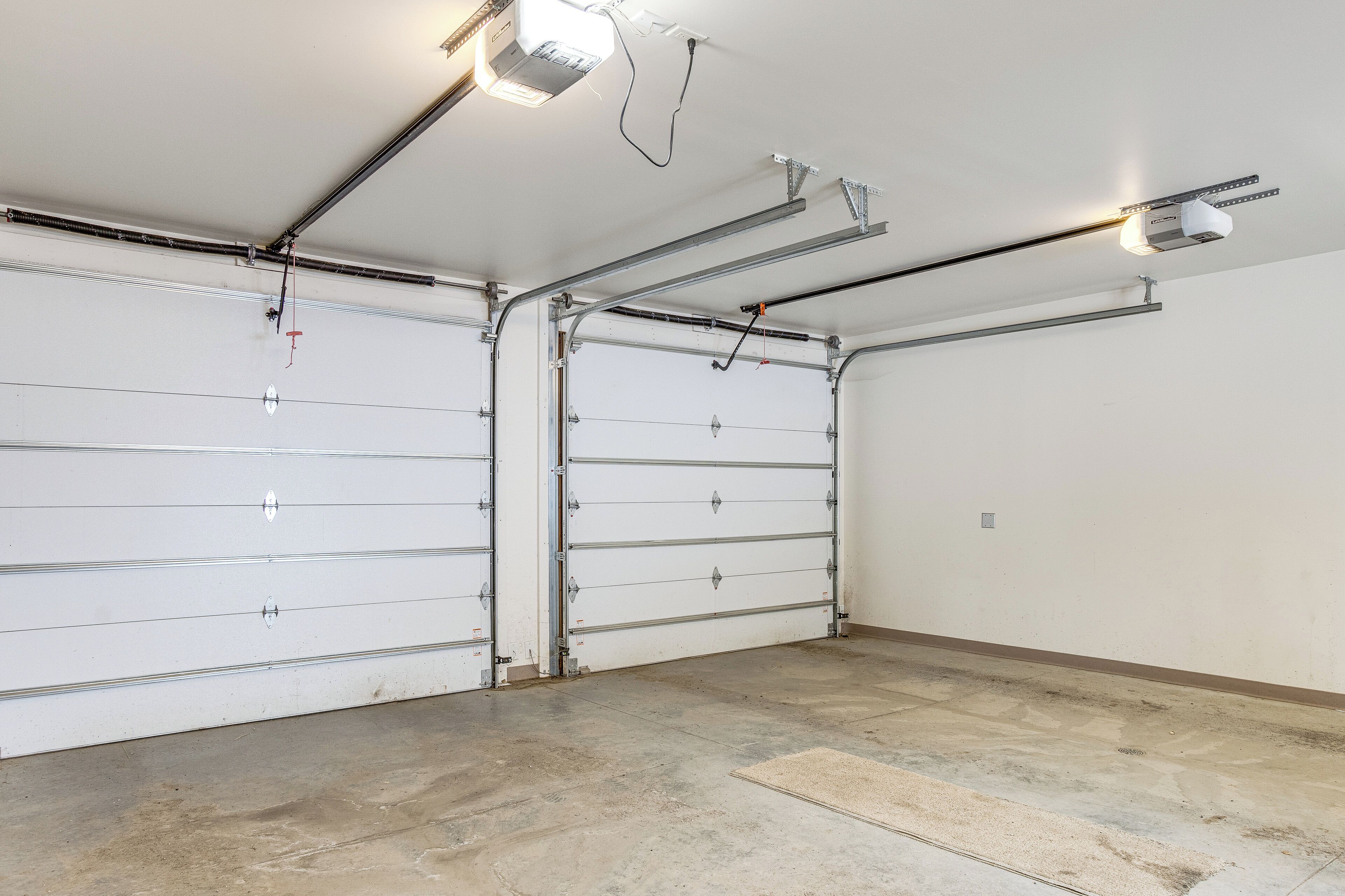 A garage with two white garage doors, overhead lighting, and a concrete floor.