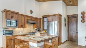Cocina con armarios de madera, refrigerador de acero inoxidable, microondas y una isla grande con taburetes.