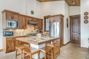 Eine Küche mit Holzausstattung, einem Edelstahlkühlschrank, einer Mikrowelle und einer großen Kochinsel mit Barhocker.