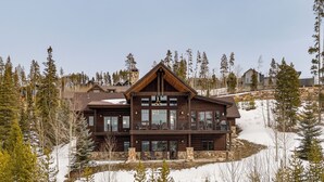 Un amplio lodge de madera con varios balcones, rodeado de árboles cubiertos de nieve y un cielo despejado.