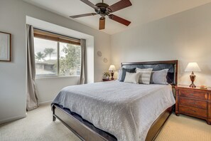 Ein Schlafzimmer mit einem Bett, einem Deckenventilator, einem Nachttisch mit Lampen und einem Fenster mit Vorhängen.