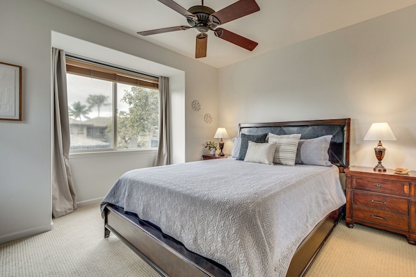 A bedroom with a bed, a ceiling fan, a nightstand with lamps, and a window with curtains. - Beach Club & Pool at Big Island Resort Getaway! (Waimea)