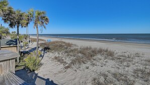 Blick auf einen Strand mit einer Holzterrasse, Palmen und Sand.