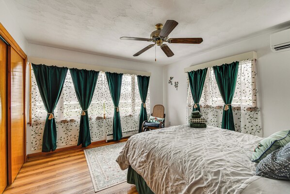 A bedroom with a bed, a ceiling fan, a window with curtains, a chair, and a rug.