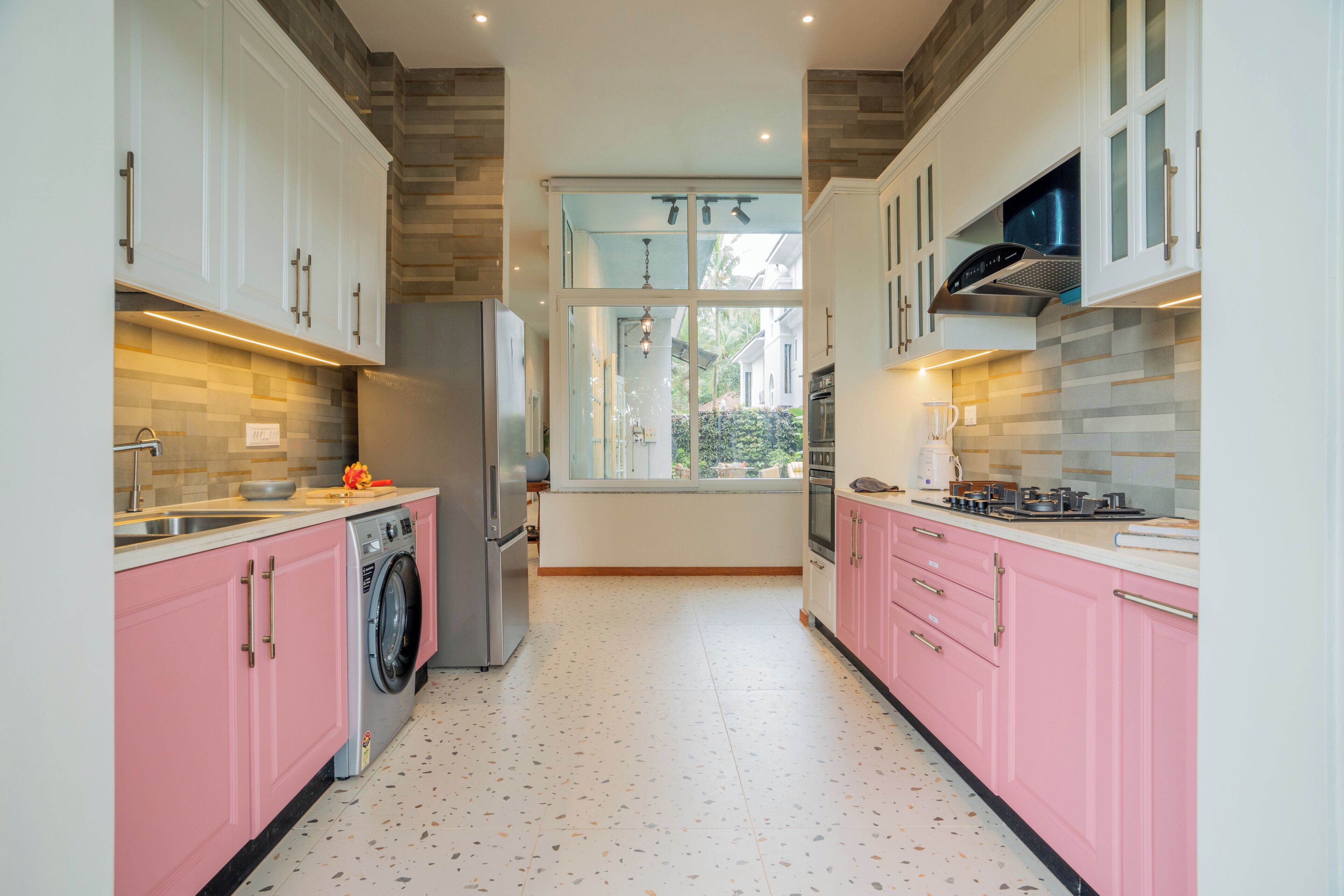 A modern kitchen with white and pink cabinets, a washing machine, and a large window providing natural light.