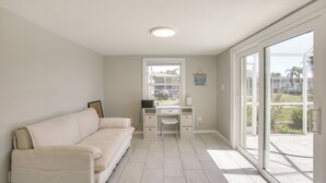 Une pièce avec un canapé blanc, un bureau avec une chaise, une fenêtre et une vue sur l’extérieur.